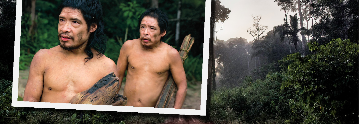 Photo of two Indigeneous people carrying wood against backdrop of Amazon Rainforest