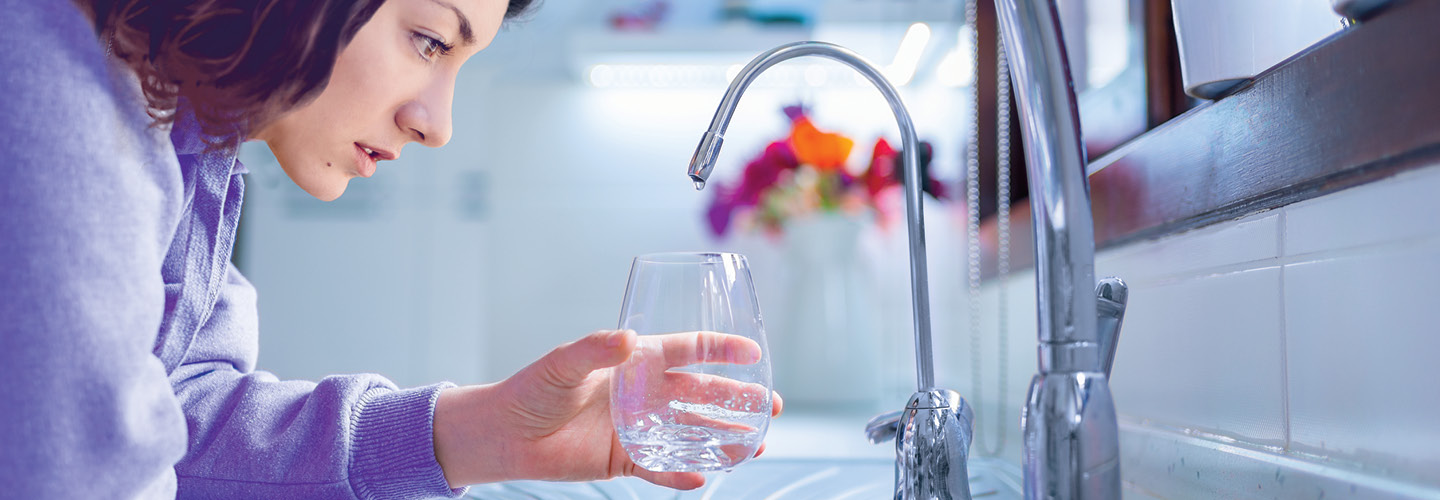 Image of a person holding glass below kitchen sink faucet for water