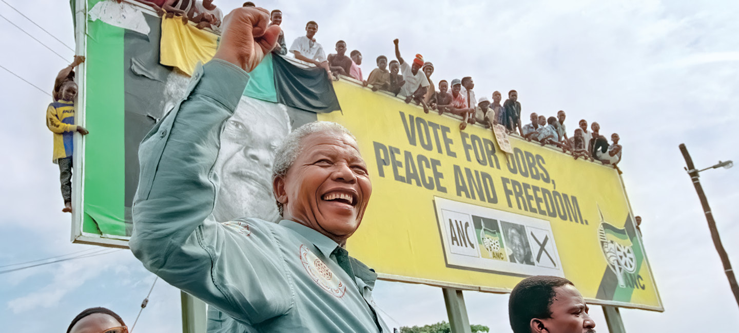 Photo of Nelson Mandela cheering against background saying, "Peace and Freedom"