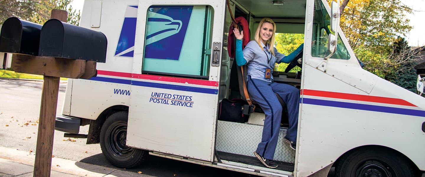 Photo of a U.S. postwoman waving from her mail truck